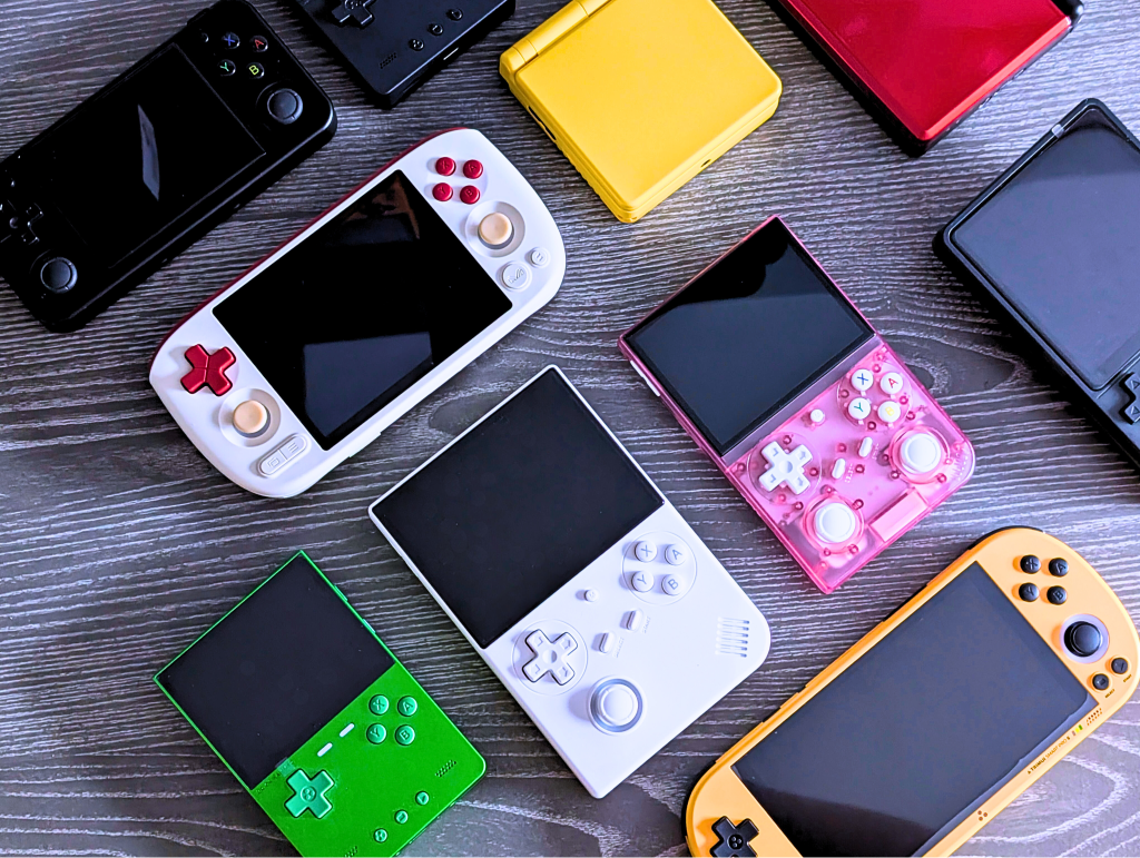 Collection of colorful handheld gaming consoles on table.