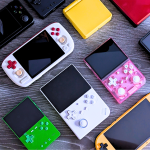 Collection of colorful handheld gaming consoles on table.